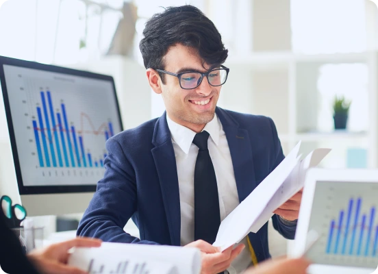 A focused professional in a suit analyzes documents while seated at a desk with graphs on computer screens in a bright office setting.checking Letting Agents for Landlord.